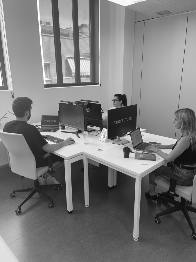 Imagen en blanco y negro donde se pueden ver tres trabajadores de Bihotz Studio sentados en las mesa de su oficina