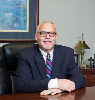 Attorney Ron sitting at his desk. He is wearing a suit and has glasses on.