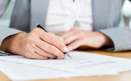 A woman writing on a document at her desk.