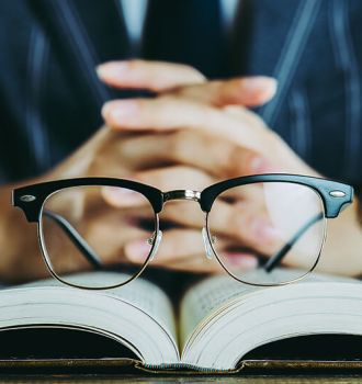 Businessman with his hands folded with open book and glasses