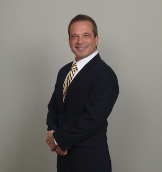 Attoney John Larson standing with his arms crossed and smiling. He is wearing a black suit.