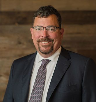 Eric J. Burch in a black suit against a wood background