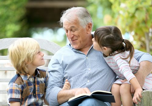 A grandpa reading to his two grandchildren in the park.
