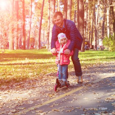 A father helping his daughter ride a scooter in the park.