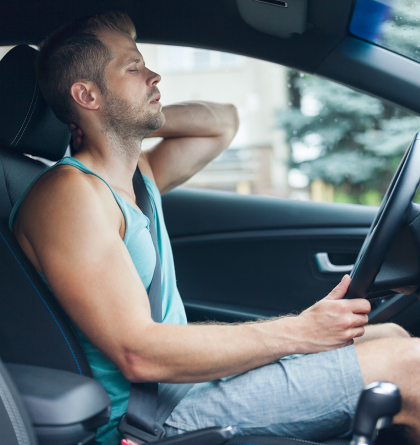 A man holding his neck in pain while in his car.