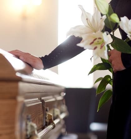 A woman holding lilies, with her hand resting on a casket.