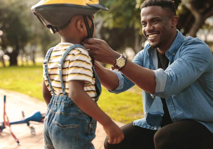 a black man helping his son put on a bicycle helmet