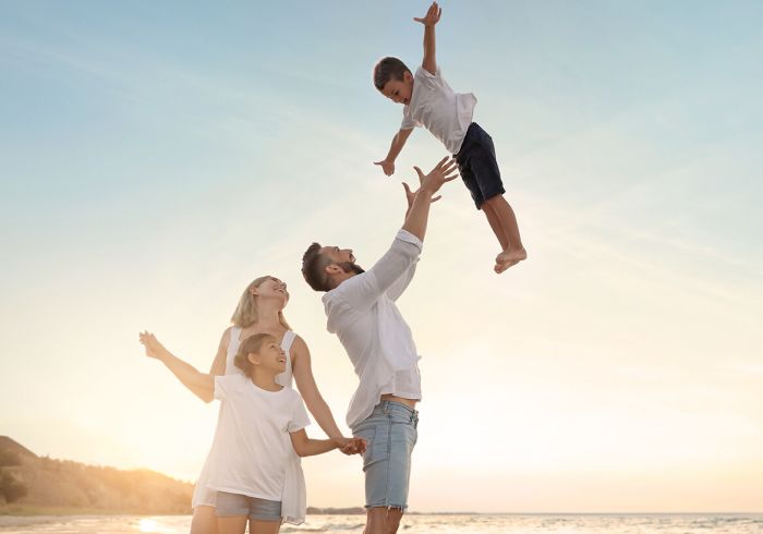 Father tossing up son in the air while mother and sister look on