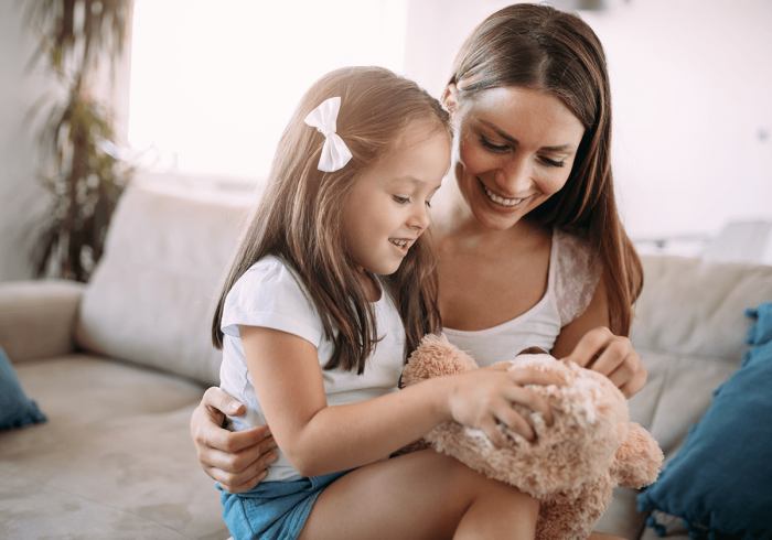 A mother playing with a teddy bear with her daughter.