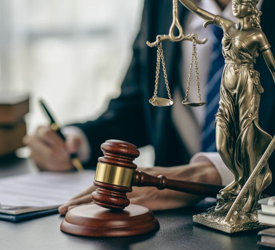 An attorney writing at his desk with a gavel and a lady of justice statue.