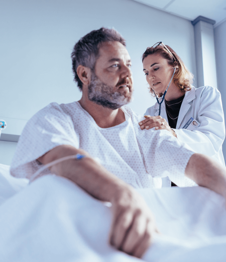 A female doctor listening to a man's heartbeat in a hospital bed.