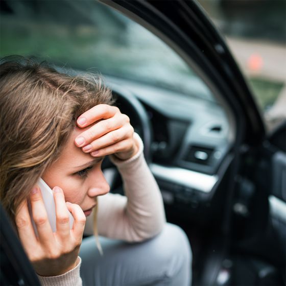 Young woman in the damaged car after a car accident, making a phone call.