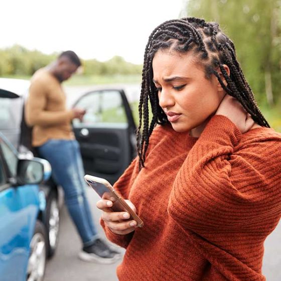 woman looking at her phone and holding her neck after a car accident