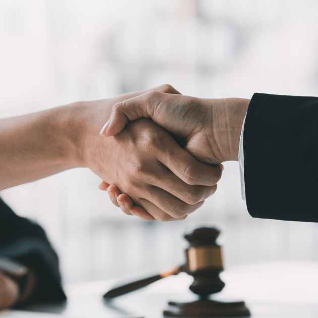 Close-up view of wooden hammer and lawyer with client shaking hands behind