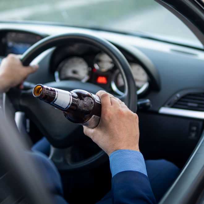 man in an expensive suit drinks beer at the wheel of a car causing the danger of an emergency.