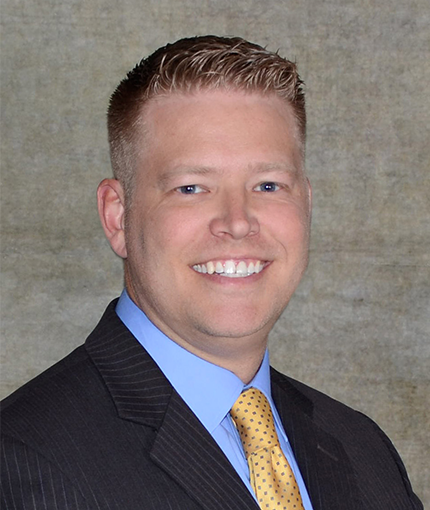 Nicholas Heiman smiling in black suit with yellow tie