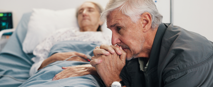 An elderly man looking distressed while his wife is laying in a hospital bed
