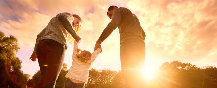 Parents swinging their daughter by her arms.