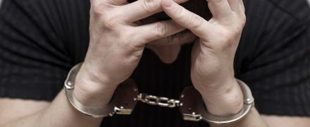 A man hold his head after being handcuffed.