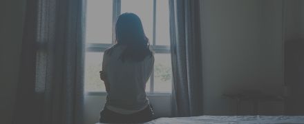 woman sitting on bed in room with light from window