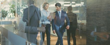 Businessman and Businesswoman Walking Through Glass Hallway