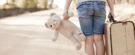 A young girl with her suitcase and stuffed teddy bear traveling to new foster care location
