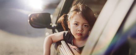 A small girl looking sad in a car window