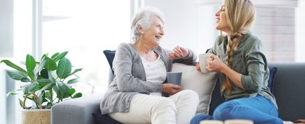 A woman talking with her grandma, with mugs in their hands.