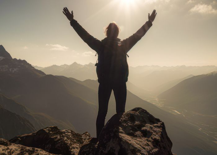 A person reaching the top of a mountain with the sun beaming on them.