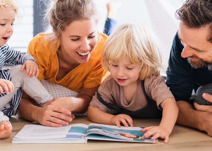 Young family with two small children indoors in bedroom reading a book.