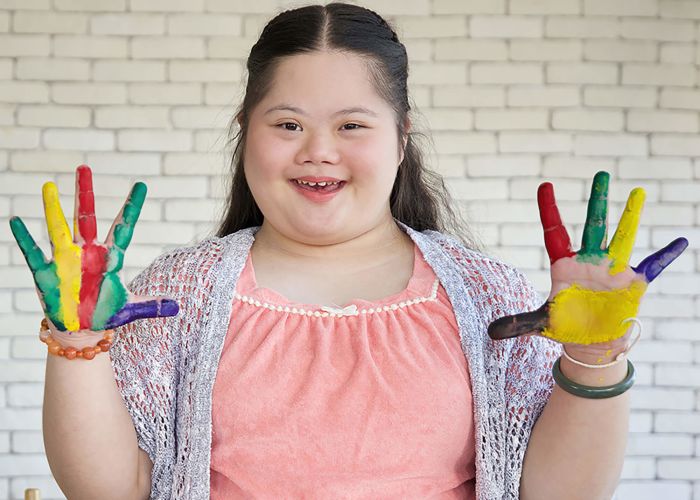 down syndrome teenage girl showing painted hands, drawing a picture on paper