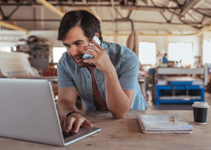 Smiling woodworker discussing designs over a cellphone and working online