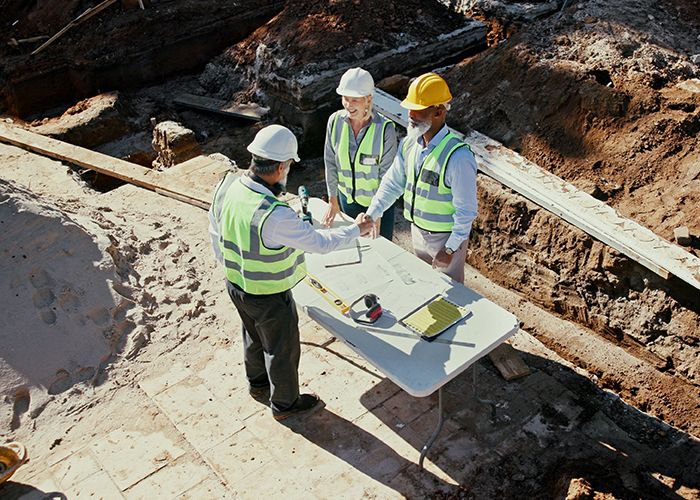 Construction team, handshake and engineer people in partnership outdoor with foundation blueprint.
