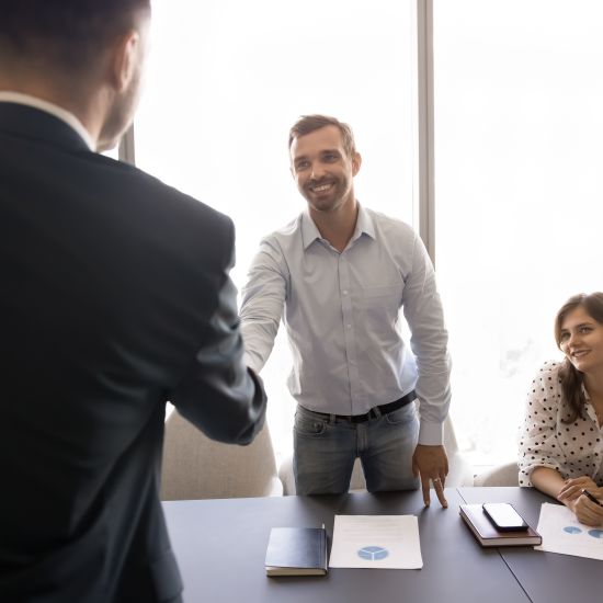 Two smiling millennial businessmen, partners, shareholders shaking hands before negotiations meeting, expressing mutual respect