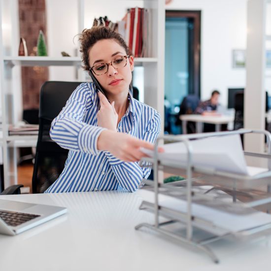 Young lady at desk doing paperwork and talking on smartphone.