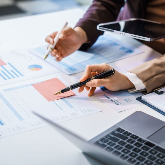 Two female business professionals in suits sit at desk, engaged in strategic discussion.