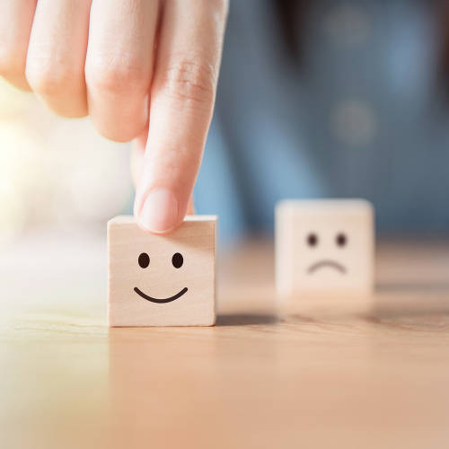 Man picking up block with smile face on it while a block with a frown on it sits in the background