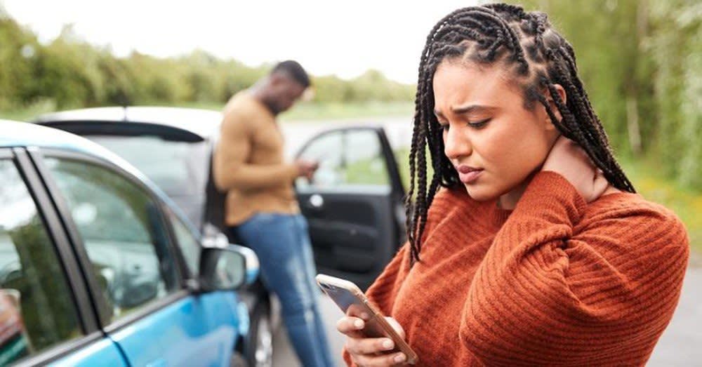 Woman holding her neck in pain after a car accident. Man leaning on his car