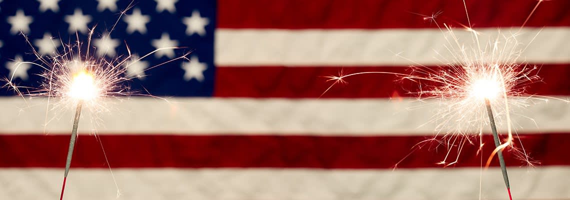 Two sparklers are held in front of an American flag