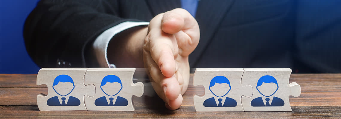 Person with hand dividing puzzle pieces with model figures on desk
