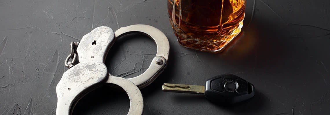 Handcuffs next to glass of alcohol and key