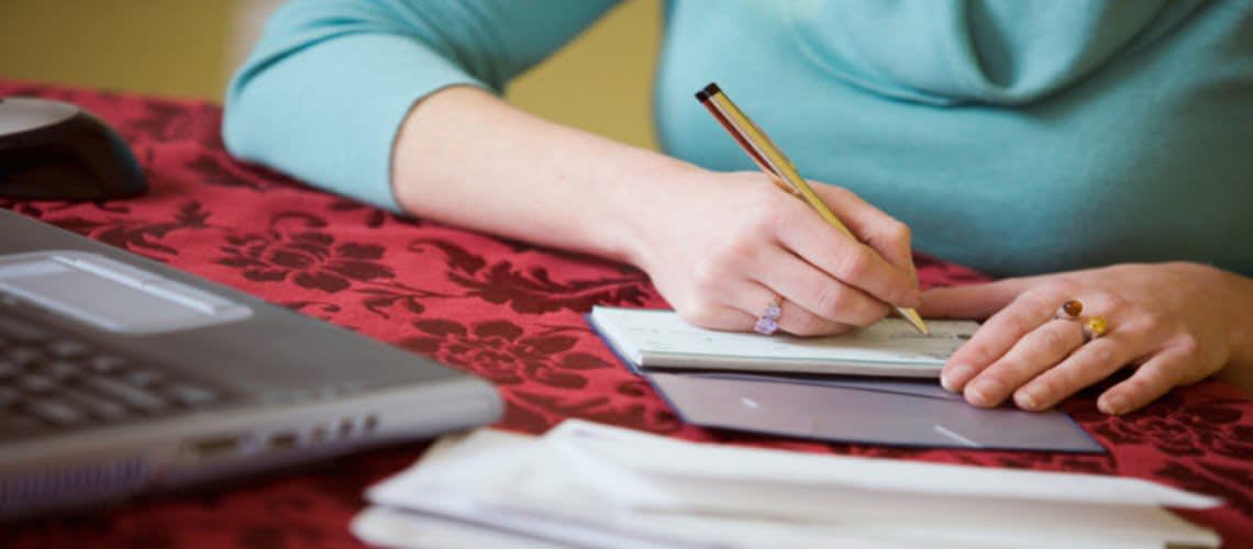 Woman writing checks by a laptop