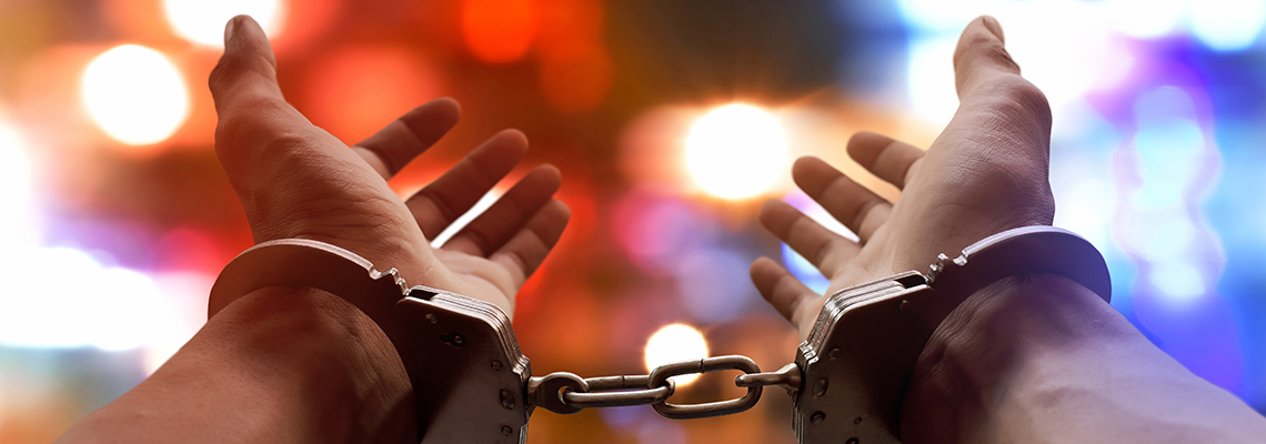 A man wears handcuffs in front of police car lights
