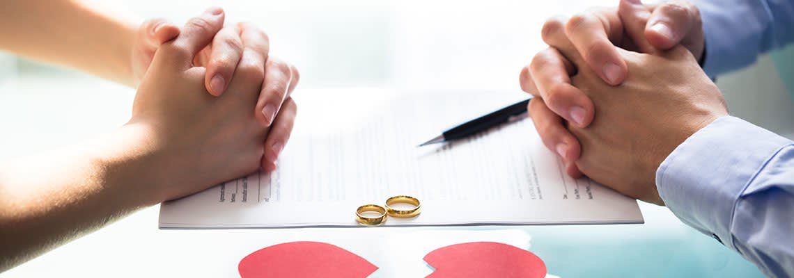 Couple resting hands on divorce document next to rings and a broken heartCouple resting hands on divorce document next to rings and a broken heart