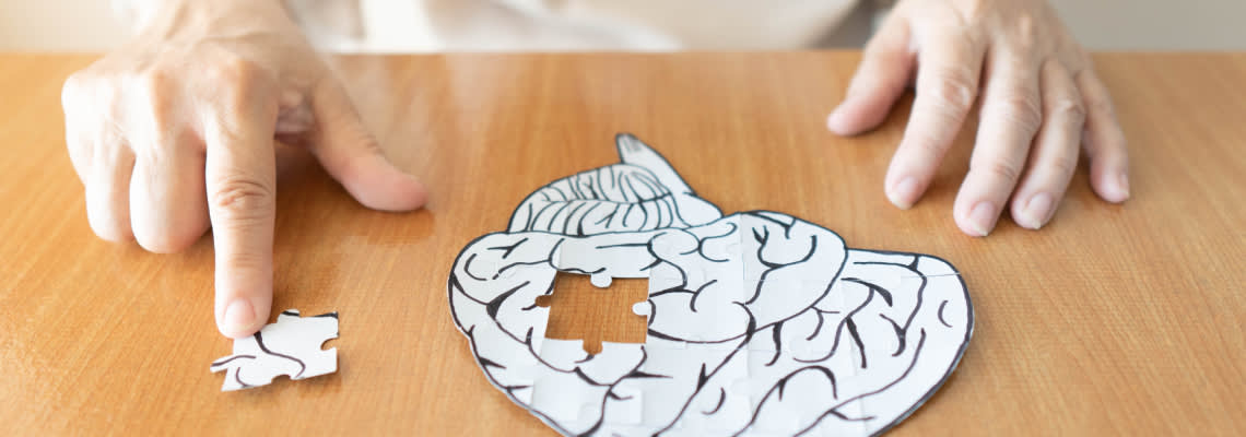 Elderly hands solving puzzle in shape of human brain