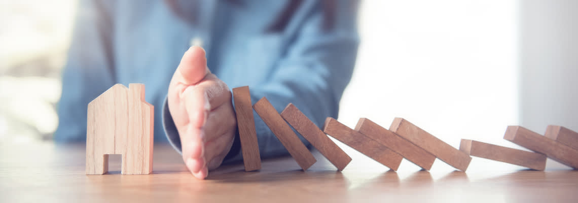 Women stopping wooden blocks from falling on house model