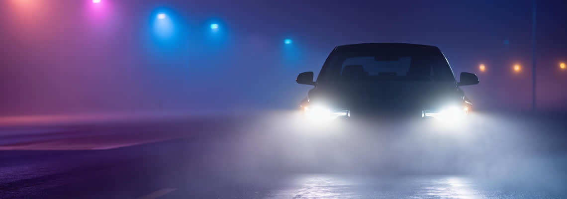 Car driving through fog at night with headlights illuminating the misty road