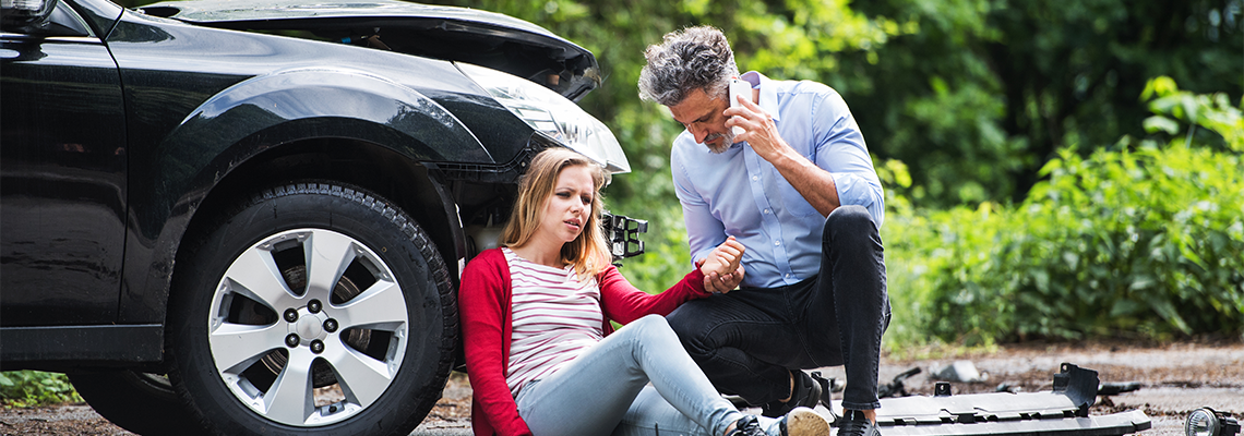 Two people sitting by a car after an accident