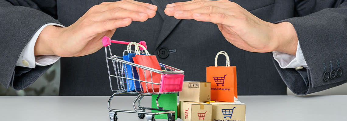 Businessman holding hands above miniature shopping bags and cart