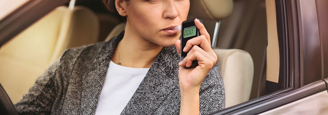 A woman blows into a blood alcohol reader in her car